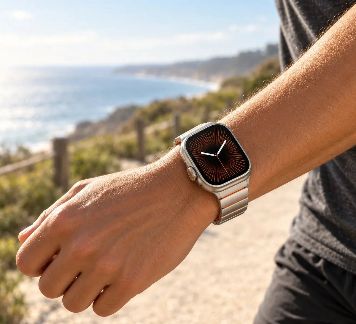 Silver smartwatch band worn on a wrist outdoors near the coast.